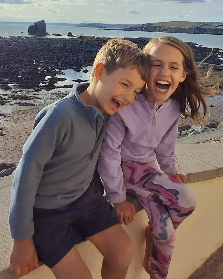 Alan's children, Joshua and Abigail, laughing together on a beach wall