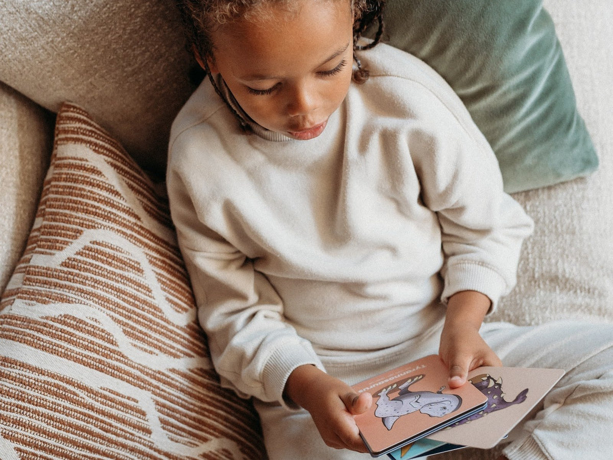 A child curled up on a sofa looking through her flashcards