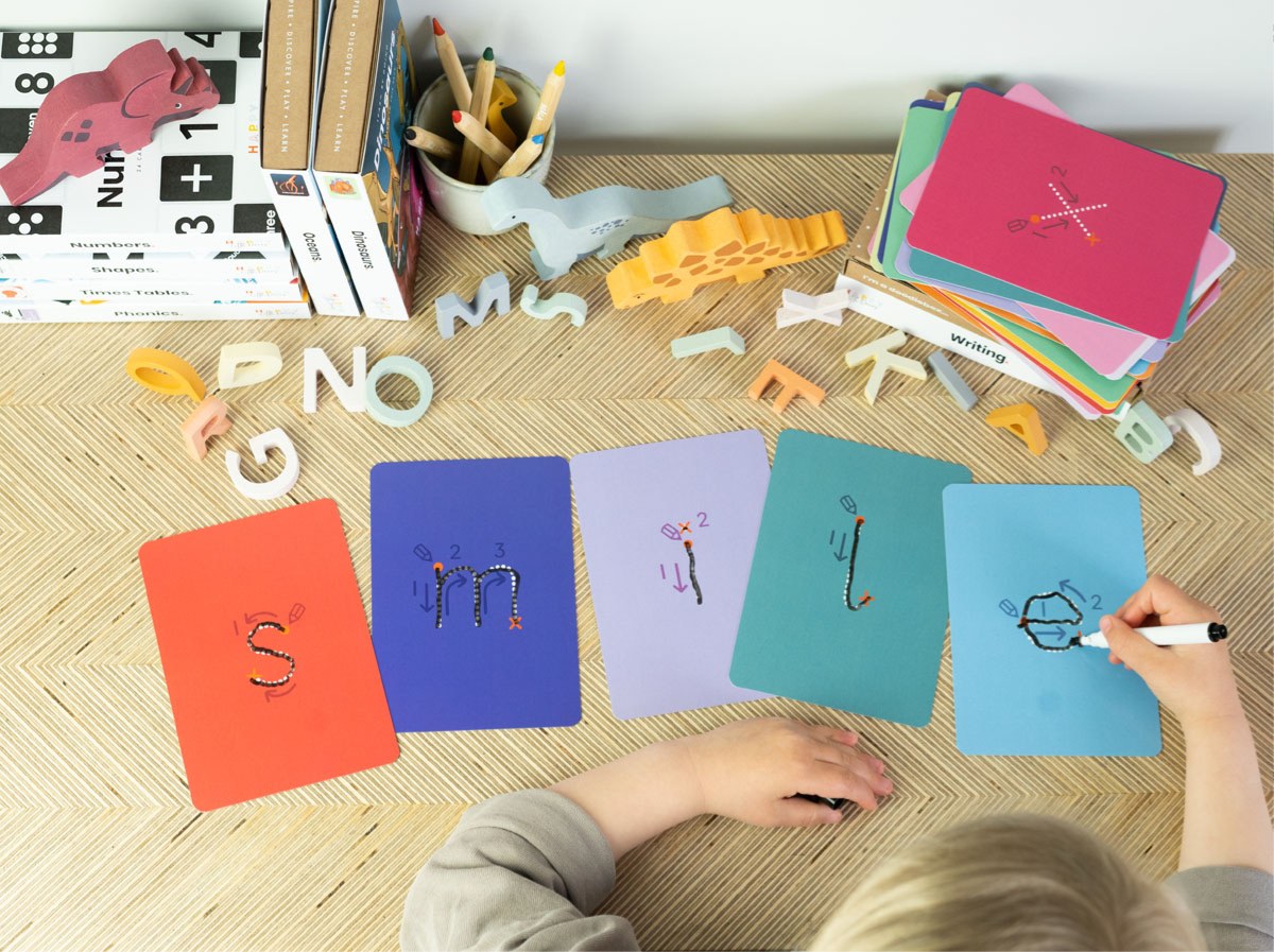 A child tracing letters on a wipe-clean Writing Flashcard