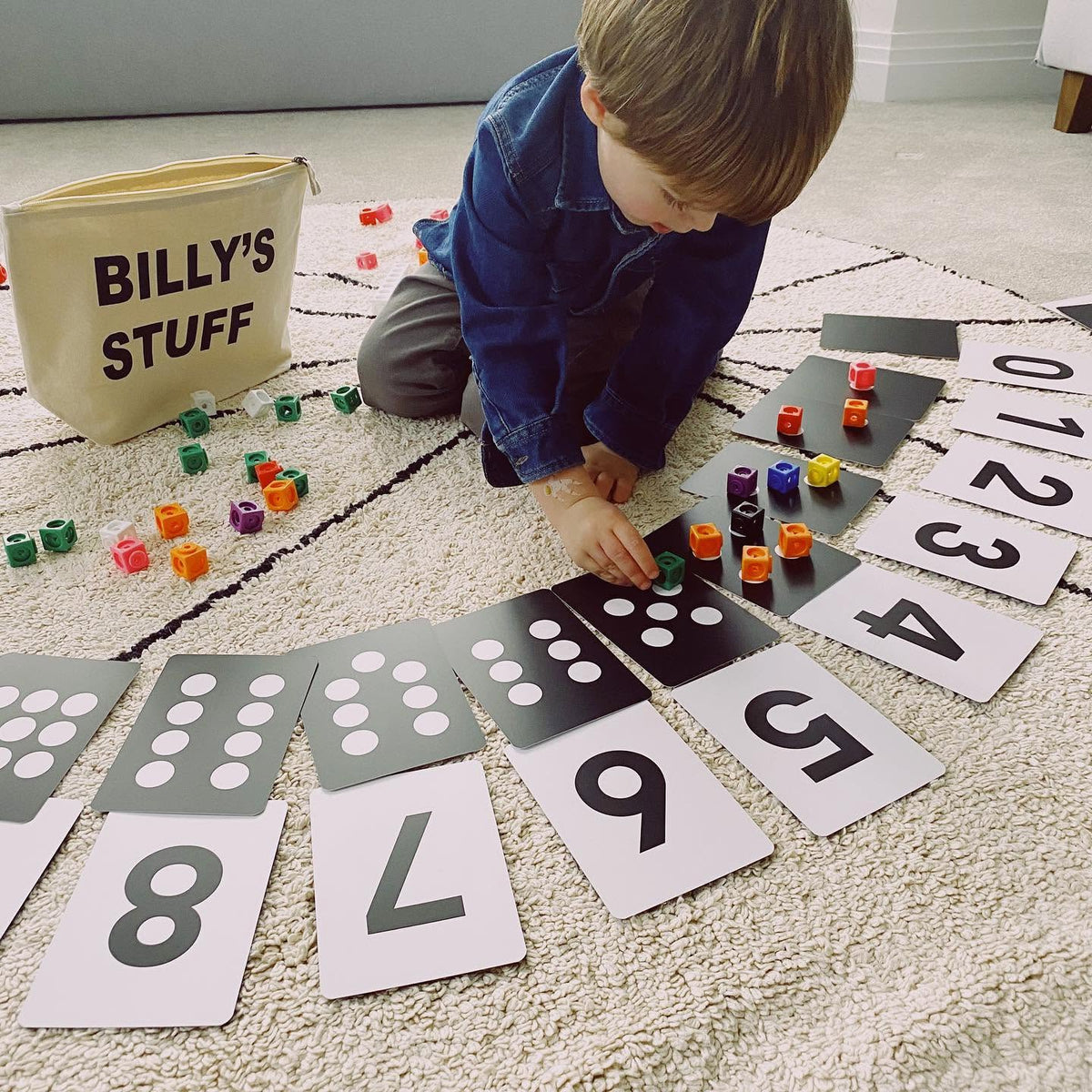 A child placing coloured counters on the dots of Numbers flashcards laid out on a rug